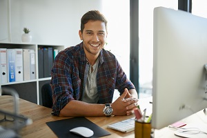 Man smiling with hands clasped in front of computer
